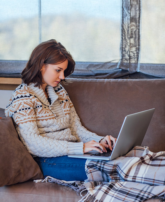 Woman sits on a couch using a laptop.